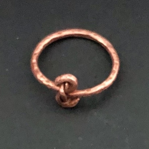 May include: A hammered copper ring with a knot design.