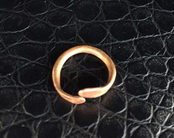 Op de afbeelding: Een koperkleurige metalen ring met een open bypass-ontwerp. De band heeft een glad, afgerond oppervlak met een warme, metallic afwerking en twee licht taps toelopende uiteinden die elkaar niet raken.