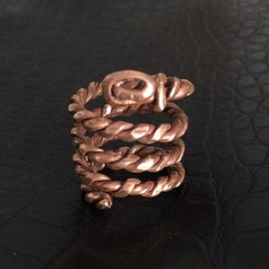 May include: A copper ring with a twisted design. The ring is made of multiple strands of copper wire that are twisted together to create a spiral shape.