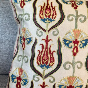 May include: A white pillow with a traditional Turkish design embroidered in red, blue, green, and gold thread. The design features stylized tulips and floral motifs.