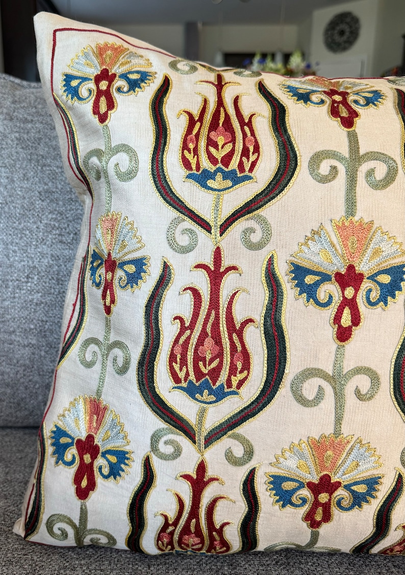 May include: A white pillow with a traditional Turkish design embroidered in red, blue, green, and gold thread. The design features stylized tulips and floral motifs.