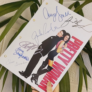 Può includere: Uno script bianco con il titolo "Pretty Woman" in lettere rosa e rosse. Lo script è firmato da Julia Roberts, Richard Gere, Laura San Giacomo e Jason Alexander.