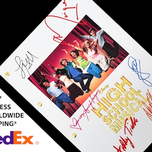 Peut inclure: Un script blanc avec le titre "High School Musical" en lettres colorées avec un groupe d'acteurs sautant devant un rideau rouge. Le script est signé par Zac Efron, Vanessa Hudgens, Ashley Tisdale et Corbin Bleu.