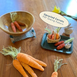 Może przedstawiać: Zestaw czterech filcowych marchewek w drewnianej misce, koszyk z filcowymi marchewkami i dwa filcowe króliki. Marchewki są pomarańczowe i mają zielone czubki. Króliki są białe z różowymi noskami. Tekst "Upcycled Carrots PDF Sewing Pattern" jest napisany na białym owalu.