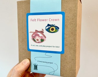 May include: A brown cardboard box wrapped in a light blue paper band featuring the text Felt Flower Crown, A cut, sew, and play project for kids!, and A hand-sewing project with a spool illustration showing two felt flower crowns.