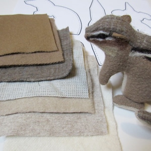 May include: A stack of different colored felt fabric squares in various shades of brown, beige, and white. The fabric is arranged in a pile, with the largest square on the bottom and the smallest square on top. The fabric is soft and fuzzy, and it would be perfect for crafting projects.