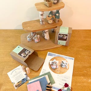 May include: A three-tiered wooden display stand with birch bark supports, featuring small felt figures, a woven basket, and an owl. Includes two cardboard boxes, a printed instruction sheet, assorted felt fabric pieces, two wooden pegs, and embroidery floss.