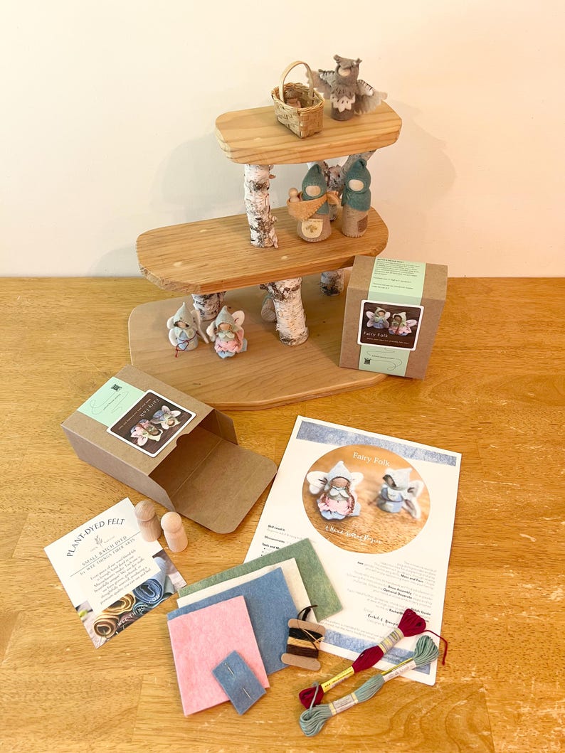 May include: A three-tiered wooden display stand with birch bark supports, featuring small felt figures, a woven basket, and an owl. Includes two cardboard boxes, a printed instruction sheet, assorted felt fabric pieces, two wooden pegs, and embroidery floss.