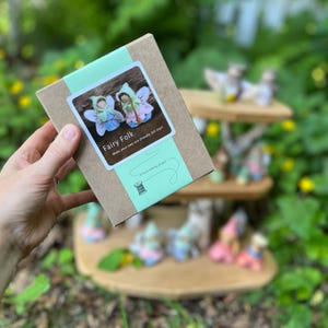 May include: A rectangular brown cardboard box with a light green paper band featuring a white label. The label displays two small felt fairy figures, the text Fairy Folk, Make your own eco-friendly felt toys, and A hand-sewing project.