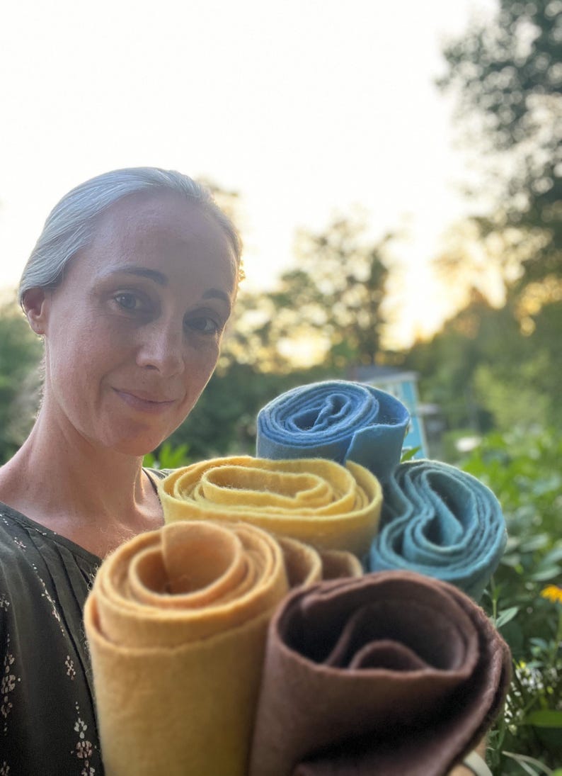 Op de afbeelding: Een close-up van opgerold vilt in verschillende kleuren: lichtbruin, geel, blauw en turquoise. Het vilt is strak opgerold, waardoor de textuur en kleurvariaties zichtbaar zijn. De achtergrond is een vage buitensc&egrave;ne.