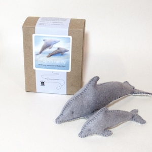 May include: A brown cardboard box with a label that says "Dolphin Family" and shows a picture of three grey felt dolphins. The box contains a felt craft kit to make your own eco-friendly felt toys.