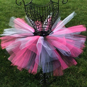 May include: A pink, white, and black tulle tutu skirt on a black metal dress form. The skirt is layered and fluffy.