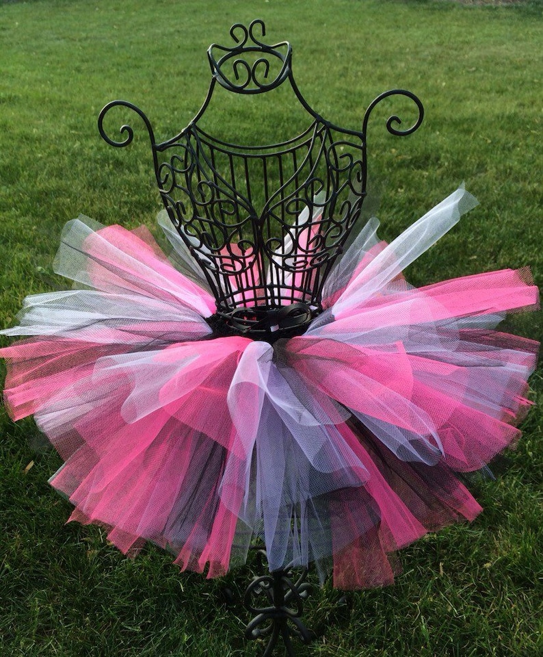 May include: A pink, white and black tulle tutu skirt on a black metal dress form. The skirt is layered and fluffy.