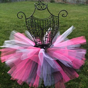 May include: A black, pink and white tulle tutu on a black metal display stand. The tutu is layered and fluffy.