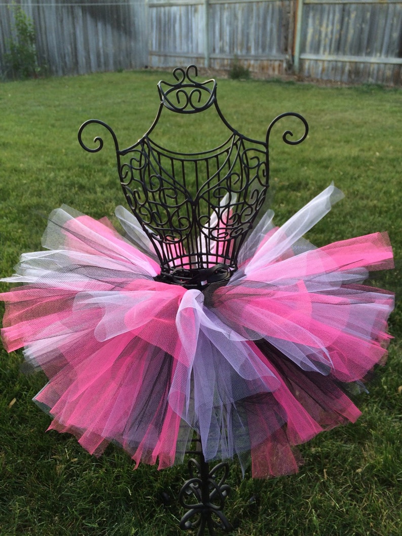 May include: A black, pink and white tulle tutu on a black metal display stand. The tutu is layered and fluffy.