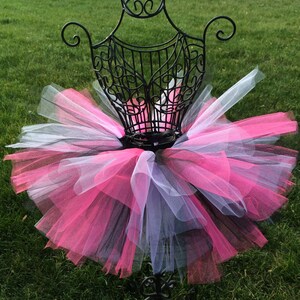 May include: A pink, black and white tulle tutu on a black metal dress form. The tutu is layered and fluffy.