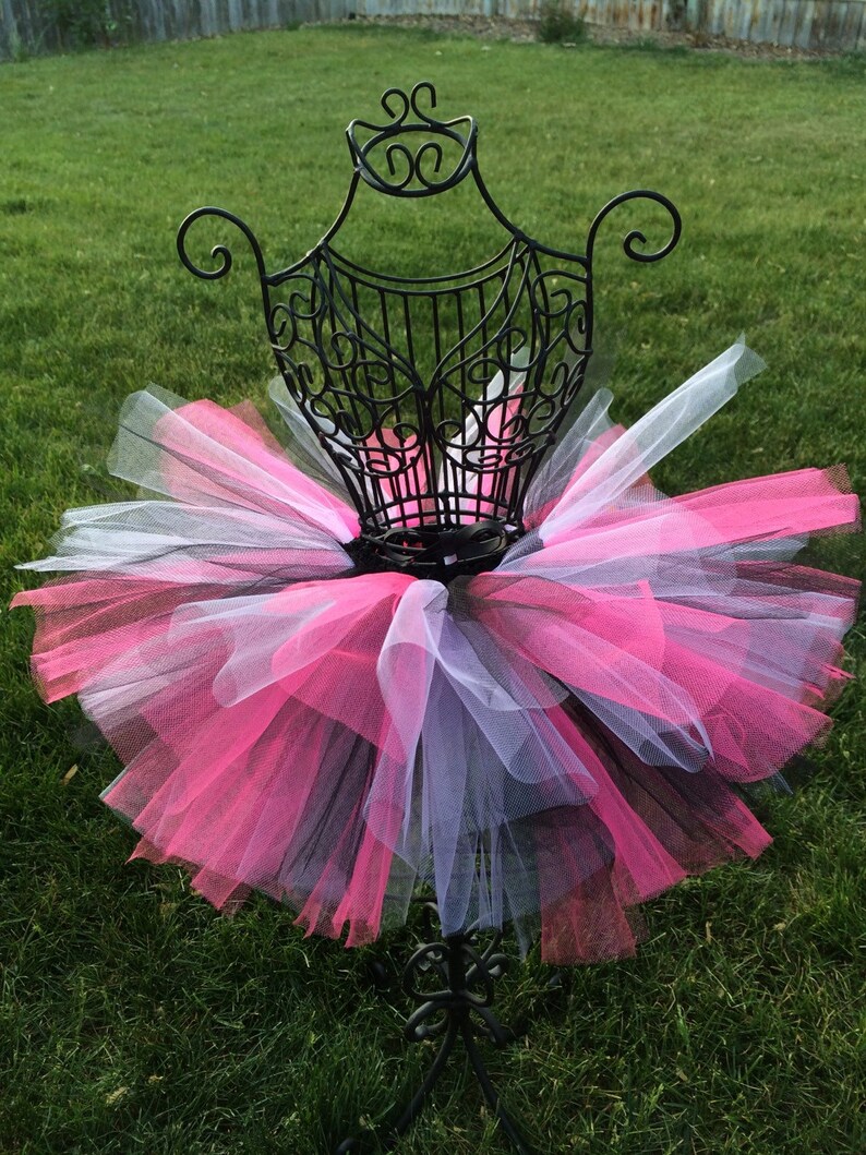 May include: A pink, black and white tulle tutu on a black metal dress form. The tutu is layered and fluffy.