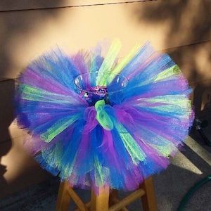 Puede incluir: Un tut&uacute; de tul colorido con capas verdes, azules y moradas. El tut&uacute; se est&aacute; utilizando como centro de mesa para un jarr&oacute;n.