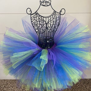 Puede incluir: Una falda de tut&uacute; de tul de varias capas en tonos de morado, azul y verde. La falda se muestra en un maniqu&iacute; de metal negro.