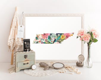 Könnte beinhalten: Ein weiß gerahmter Druck des Bundesstaates Tennessee, umrandet von floralen Designs. Der Druck ist auf weißem Hintergrund und von einem weißen Passepartout umgeben. Der Druck steht auf einem weißen Tisch mit einer Vintage-Kamera, einer kleinen Holzkiste und einer Vase mit rosa Blumen.