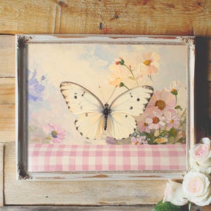May include: A framed painting of a white butterfly with black markings, perched on a pink and white gingham tablecloth. The butterfly is surrounded by delicate pink and white flowers.