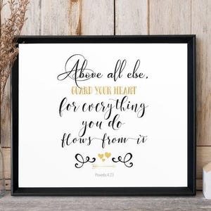May include: Black and white typography print with gold accents. The print features the quote "Above all else, guard your heart for everything you do flows from it." with the scripture reference "Proverbs 4:23".