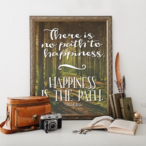 May include: A framed print with a quote about happiness. The quote reads "There is no path to happiness. Happiness is the path." The quote is attributed to Buddha. The background of the print is a photo of a forest path.