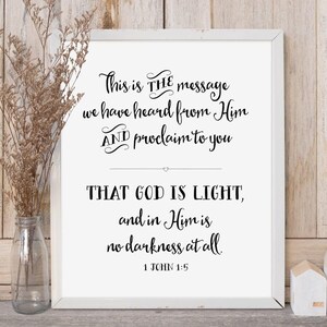 May include: A white framed print with a black and white inspirational quote from the Bible, 1 John 1:5. The quote reads "This is THE message we have heard from Him AND proclaim to you THAT GOD IS LIGHT, and in Him is no darkness at all." The print has a simple design and is perfect for home decor.