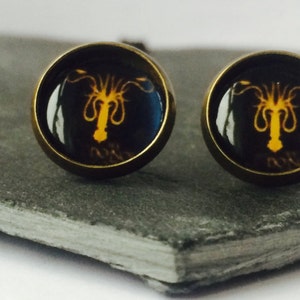 May include: A pair of cufflinks with a gold-toned metal base and a glass dome featuring a black and orange octopus design.