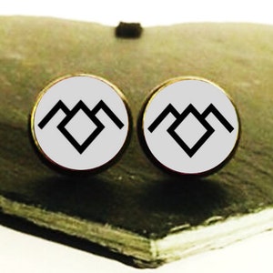 May include: A pair of white stud earrings with a black mountain symbol on each earring. The earrings are on a heart-shaped slate surface.