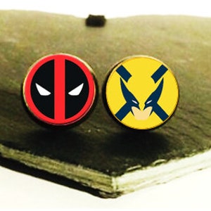 May include: Two round, metal earrings with superhero character images. The left earring features a red and black Deadpool character. The right earring features a yellow and blue Wolverine character.