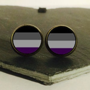 May include: A pair of earrings with a black, gray, white, and purple design. The earrings are round and have a silver-colored metal backing.