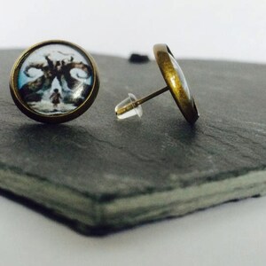 May include: A pair of bronze stud earrings with a round glass cabochon featuring a black and white image of a creature with horns.