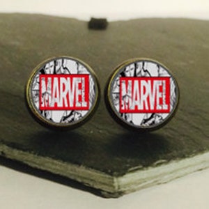May include: A pair of round, silver-toned earrings with a white and black comic book design and the word "MARVEL" in red lettering.