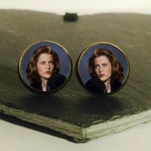 Op de afbeelding: Een paar ronde oorbellen met een foto van een vrouw met bruin haar en blauwe ogen. De vrouw draagt een donkerblauw jack en een wit shirt.