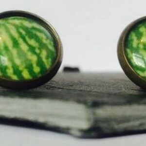 May include: A pair of green and white patterned earrings with bronze settings. The earrings are displayed on a dark grey slate surface.