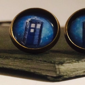 Puede incluir: Un par de pendientes Doctor Who TARDIS azules y blancos con un engaste de bronce.