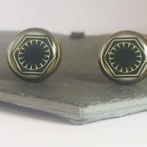 May include: A pair of gold-toned earrings with black and white glass cabochons featuring the First Order symbol from Star Wars.