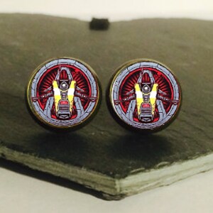 Puede incluir: Un par de pendientes redondos de madera con una imagen colorida de un robot con un traje rojo, blanco y amarillo. El robot está rodeado de un círculo plateado con una estrella roja en el centro.