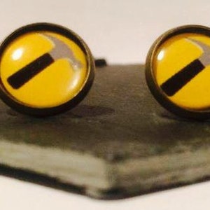 以下が含まれることがあります： ハンマーのデザインが施された、黄色と銀色のスタッドピアスのペアです。