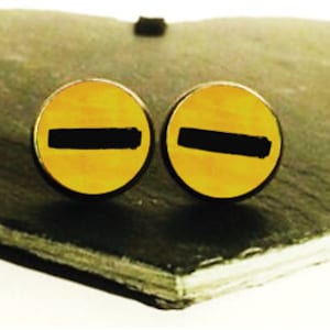 May include: A pair of yellow and black cufflinks with a horizontal black stripe design. The cufflinks are displayed on a heart-shaped slate surface.