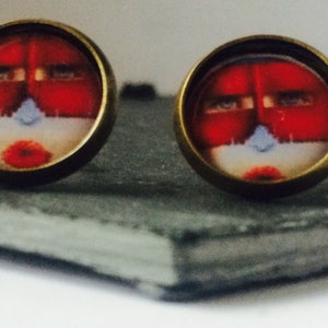 May include: A pair of earrings with a red and white face design on a dark gray background.