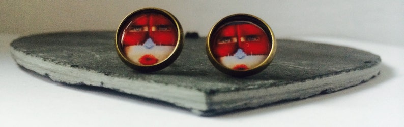 May include: A pair of earrings with a red and white face design on a dark gray background.