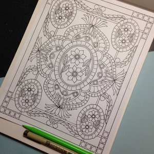 May include: A black and white coloring page featuring an intricate design of flowers, leaves, and paisley patterns. The design is framed by a border of circles.