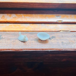 May include: A miniature white figurine of a bird with a raised tail and a small, round, shallow white bowl. Both items are solid white in colour and appear to be crafted from a smooth, matte material, presented as a set of two distinct objects.