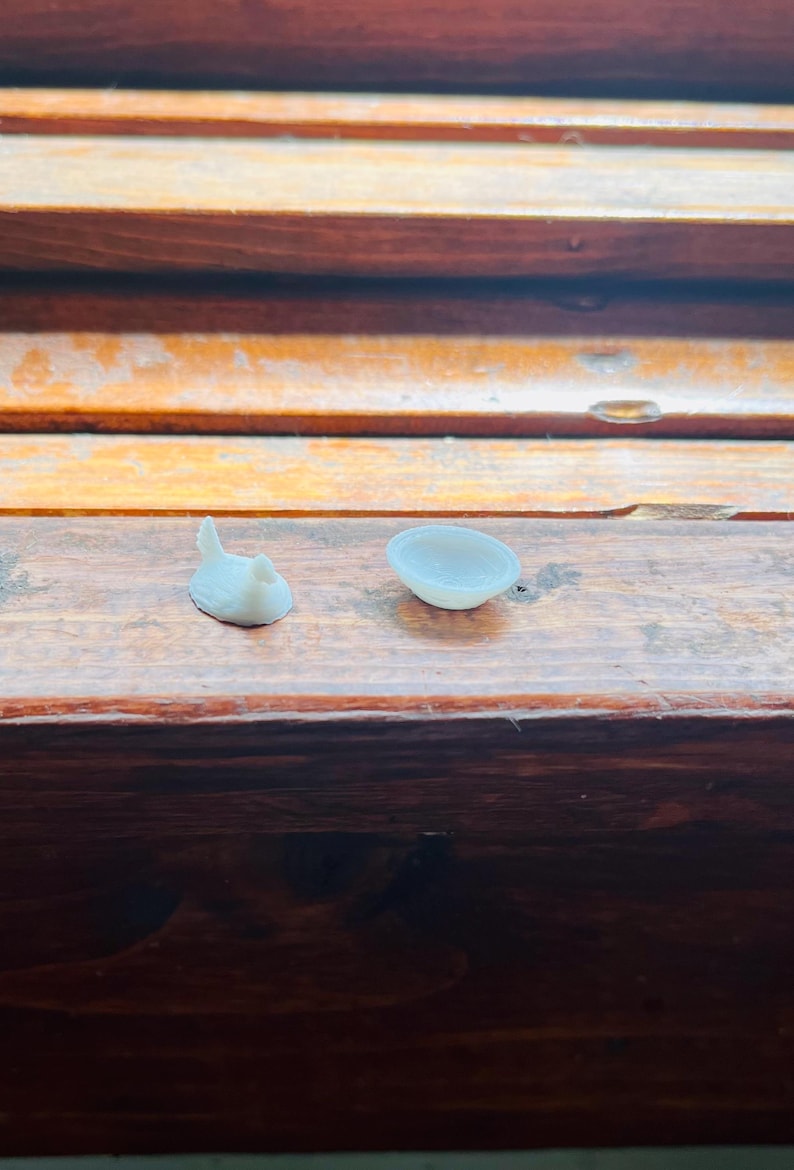 May include: A miniature white figurine of a bird with a raised tail and a small, round, shallow white bowl. Both items are solid white in colour and appear to be crafted from a smooth, matte material, presented as a set of two distinct objects.