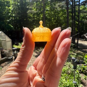 K&ouml;nnte beinhalten: Eine orangefarbene, durchscheinende Miniatur-Schatulle mit gew&ouml;lbtem Deckel und einem kleinen, zentralen knauff&ouml;rmigen Griff. Das Objekt hat eine texturierte Oberfl&auml;che und einen rechteckigen Boden, &auml;hnlich einem kleinen Dekogef&auml;&szlig; oder Spielzubeh&ouml;r.