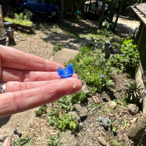 May include: A small, translucent blue duck figurine with a smooth, rounded body and a distinct beak, crafted from a lightweight material. The miniature duck is shaped in a sitting position, displaying a vibrant, solid blue colour throughout its form.