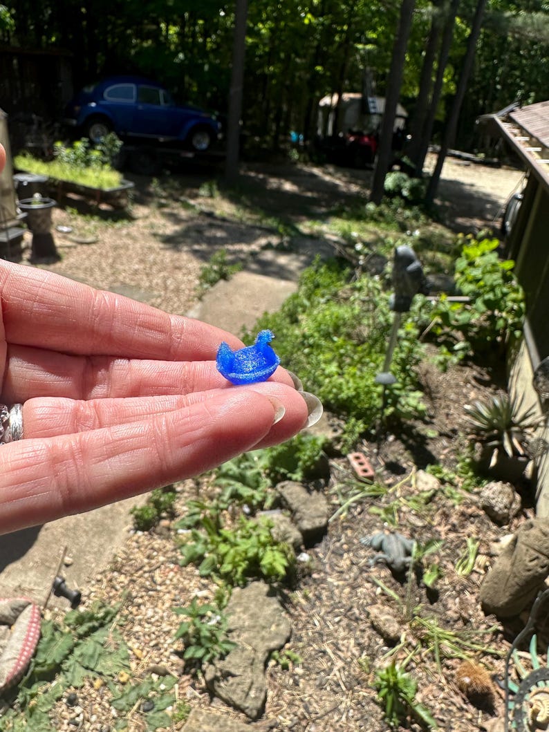 May include: A small, translucent blue duck figurine with a smooth, rounded body and a distinct beak, crafted from a lightweight material. The miniature duck is shaped in a sitting position, displaying a vibrant, solid blue colour throughout its form.