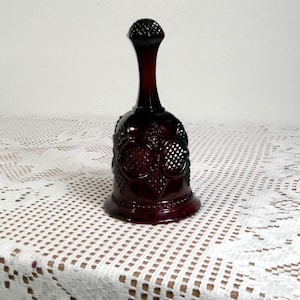 Puede incluir: Una campana de vidrio rojo rubí con una superficie texturizada y intrincados patrones florales y geométricos. La campana tiene un cuello largo y delgado y una parte superior redondeada. La campana es probablemente vintage y decorativa.